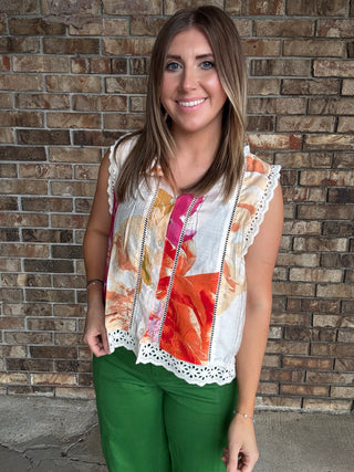Woman wearing a colorful floral sleeveless blouse with lace trim and button front