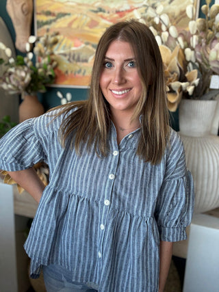 Woman wearing a gray and ivory striped tiered babydoll button-front top with dolman short sleeves