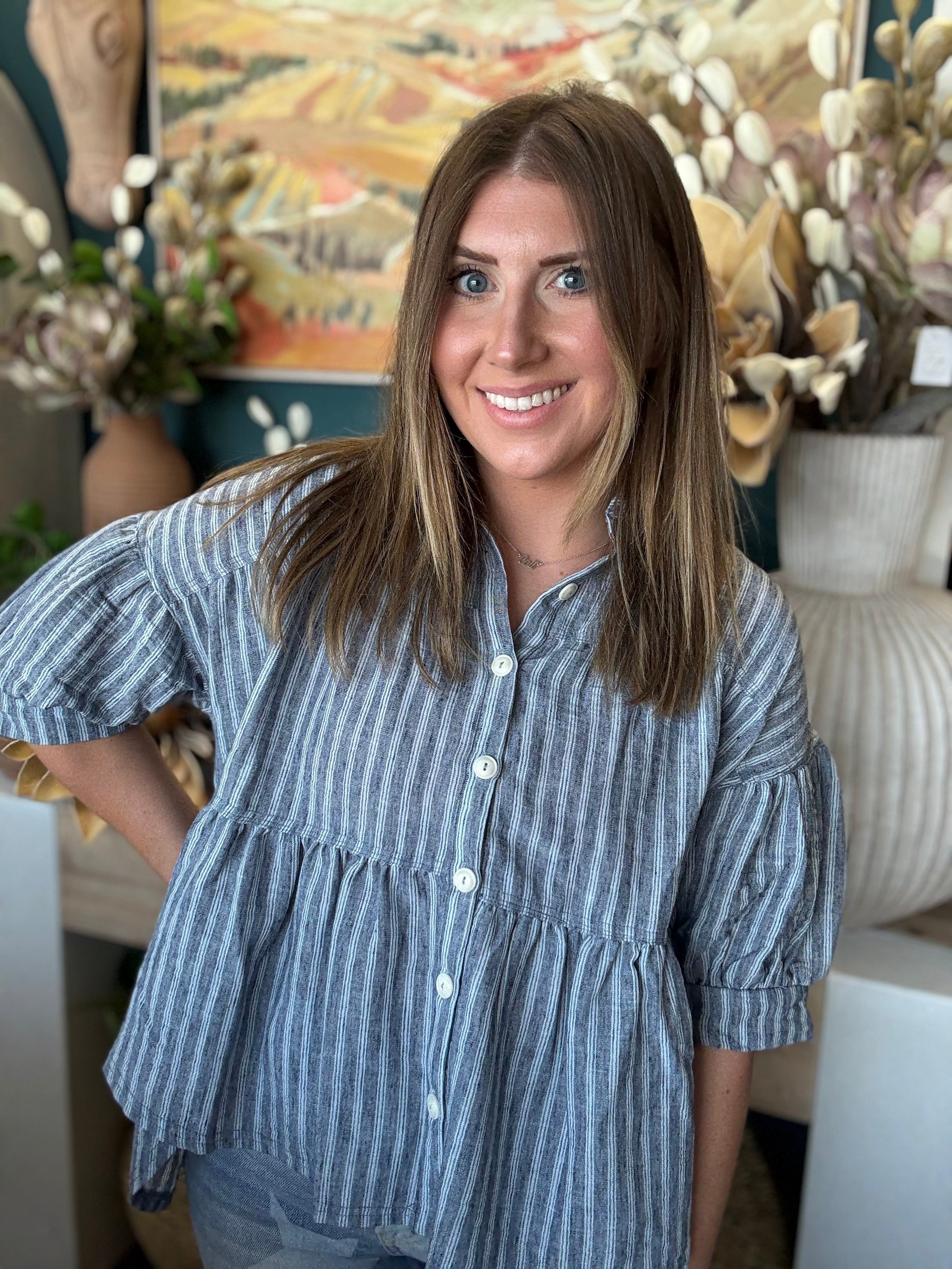 Woman wearing a gray and ivory striped tiered babydoll button-front top with dolman short sleeves