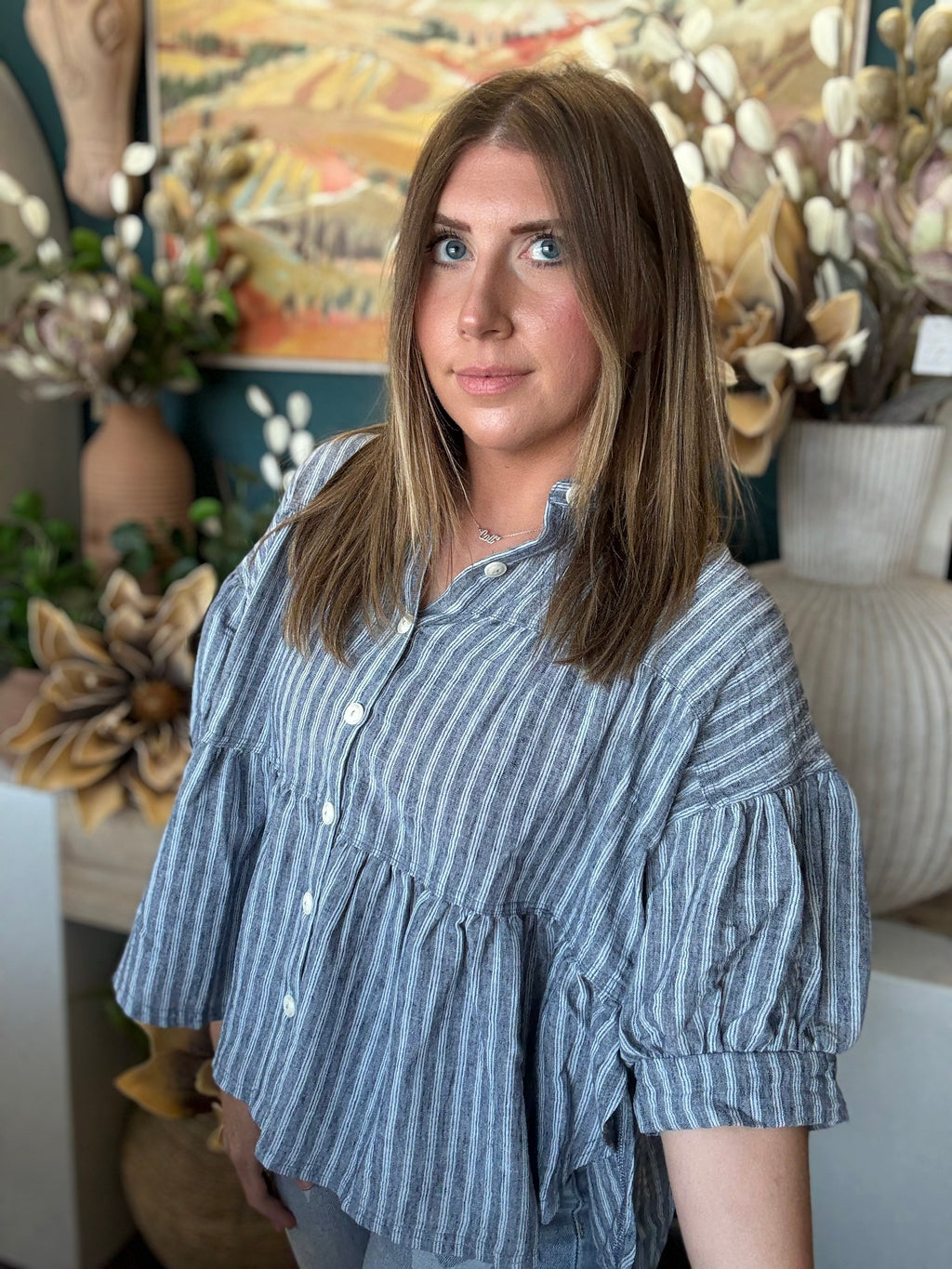 Woman wearing a gray and ivory striped tiered babydoll button-front top with dolman short sleeves