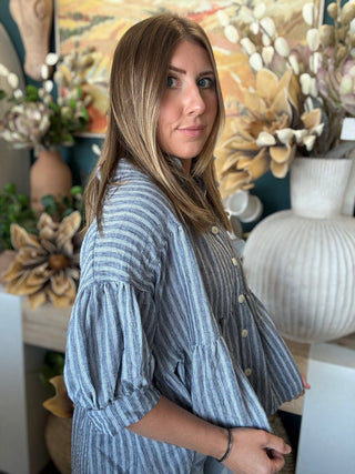 Woman wearing a gray and ivory striped tiered babydoll button-front top with dolman short sleeves