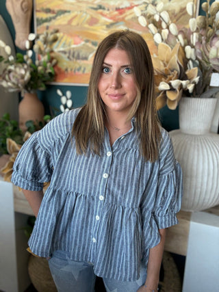 Woman wearing a gray and ivory striped tiered babydoll button-front top with dolman short sleeves