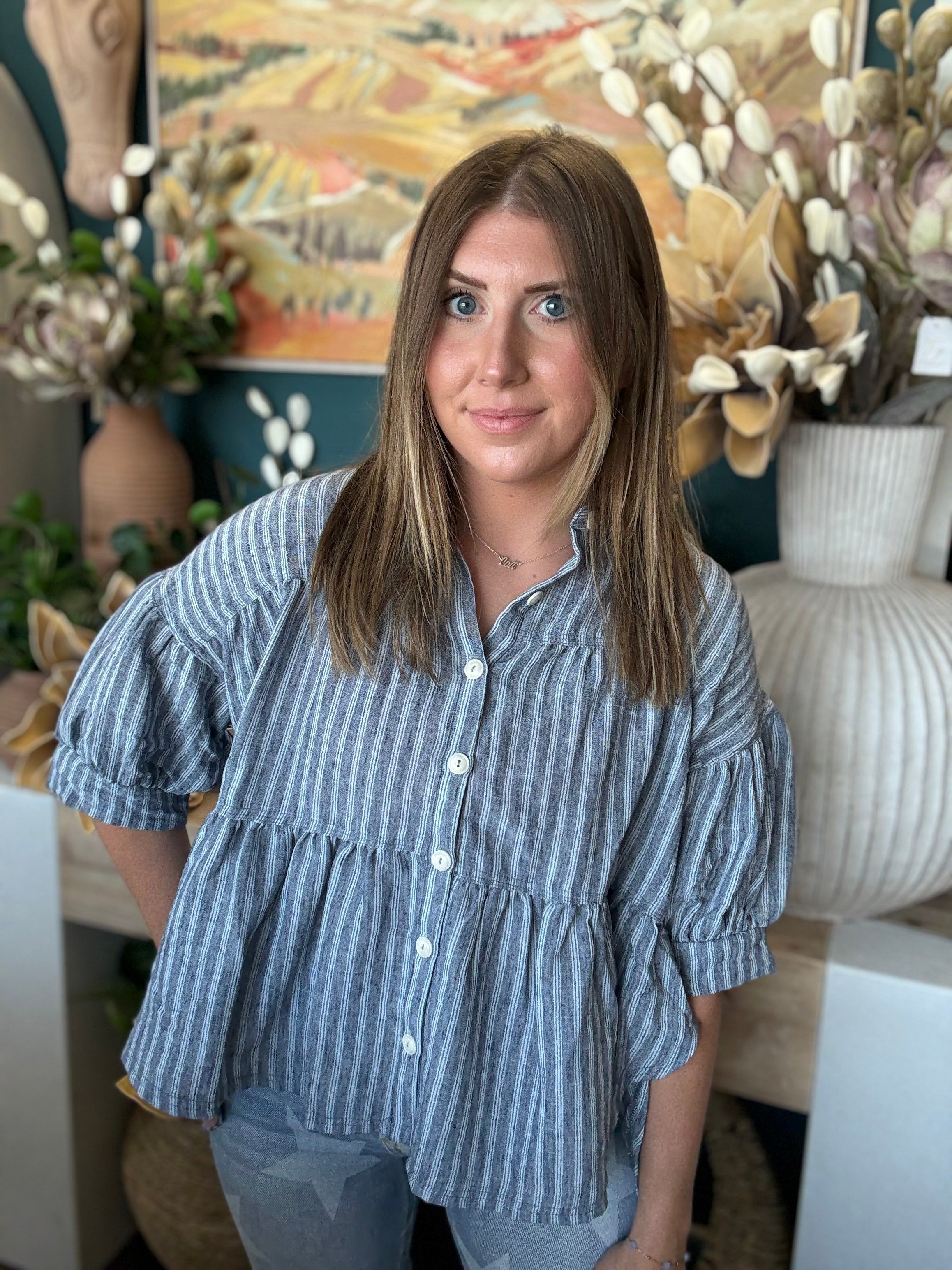 Woman wearing a gray and ivory striped tiered babydoll button-front top with dolman short sleeves