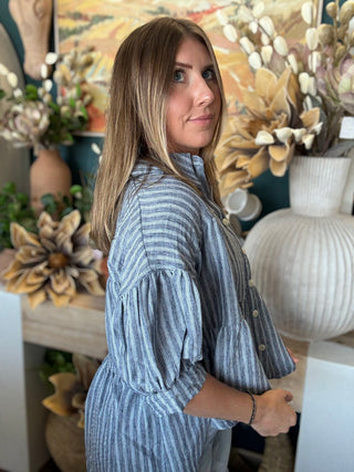 Woman wearing a gray and ivory striped tiered babydoll button-front top with dolman short sleeves