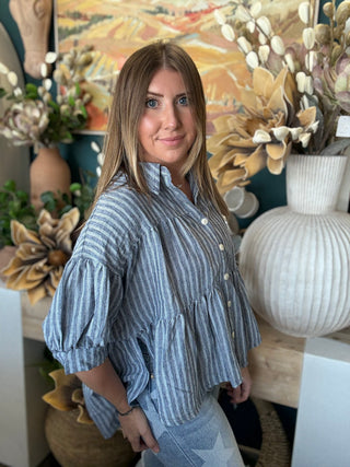 Woman wearing a gray and ivory striped tiered babydoll button-front top with dolman short sleeves