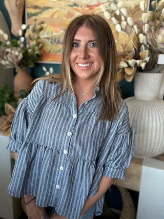 Woman wearing a gray and ivory striped tiered babydoll button-front top with dolman short sleeves