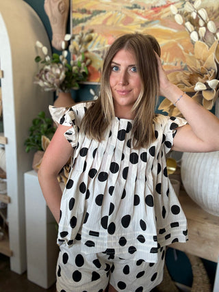 Woman wearing a black and ivory polka dot ruffle sleeve top with matching high-waisted shorts