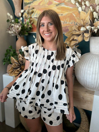 Woman wearing a black and ivory polka dot ruffle sleeve top with matching high-waisted shorts