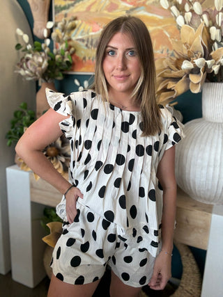 Woman wearing a black and ivory polka dot ruffle sleeve top with matching high-waisted shorts