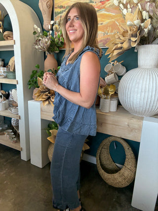 Woman wearing a dark denim chambray sleeveless top with a ruffle V-neck and relaxed babydoll silhouette