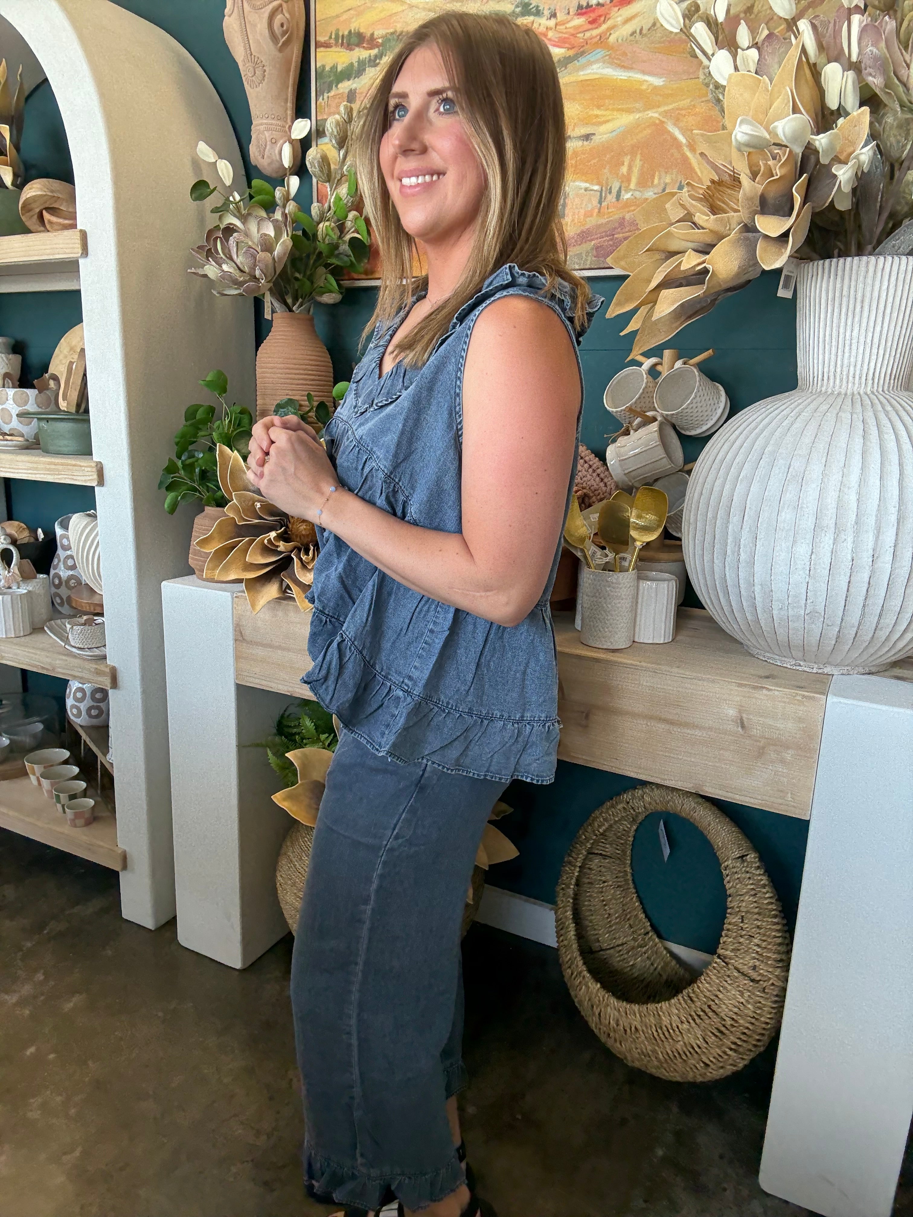 Woman wearing a dark denim chambray sleeveless top with a ruffle V-neck and relaxed babydoll silhouette