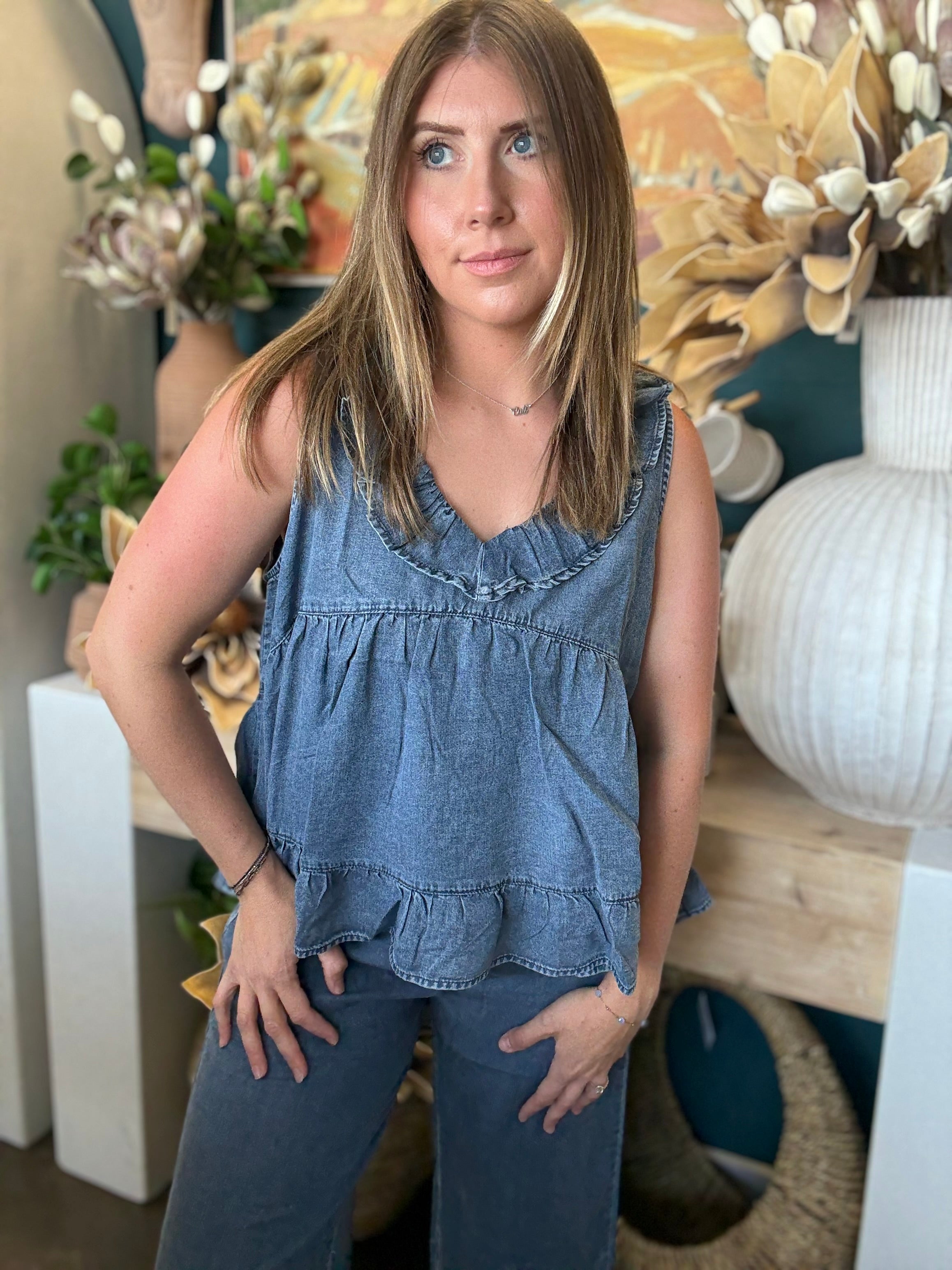 Woman wearing a dark denim chambray sleeveless top with a ruffle V-neck and relaxed babydoll silhouette