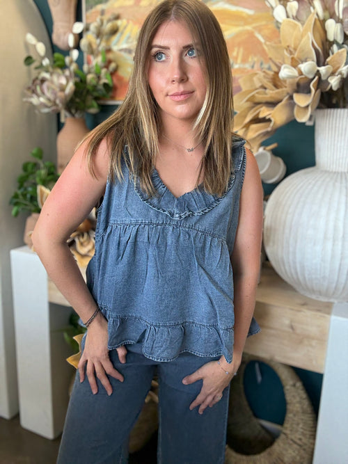 Woman wearing a dark denim chambray sleeveless top with a ruffle V-neck and relaxed babydoll silhouette