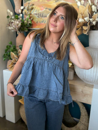 Woman wearing a dark denim chambray sleeveless top with a ruffle V-neck and relaxed babydoll silhouette