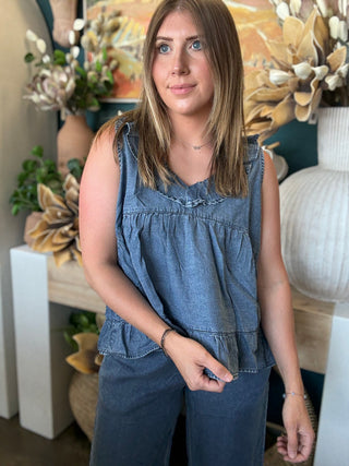 Woman wearing a dark denim chambray sleeveless top with a ruffle V-neck and relaxed babydoll silhouette