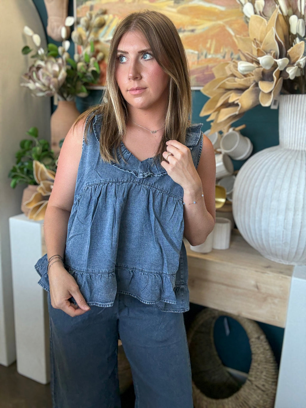 Woman wearing a dark denim chambray sleeveless top with a ruffle V-neck and relaxed babydoll silhouette