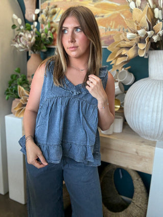 Woman wearing a dark denim chambray sleeveless top with a ruffle V-neck and relaxed babydoll silhouette