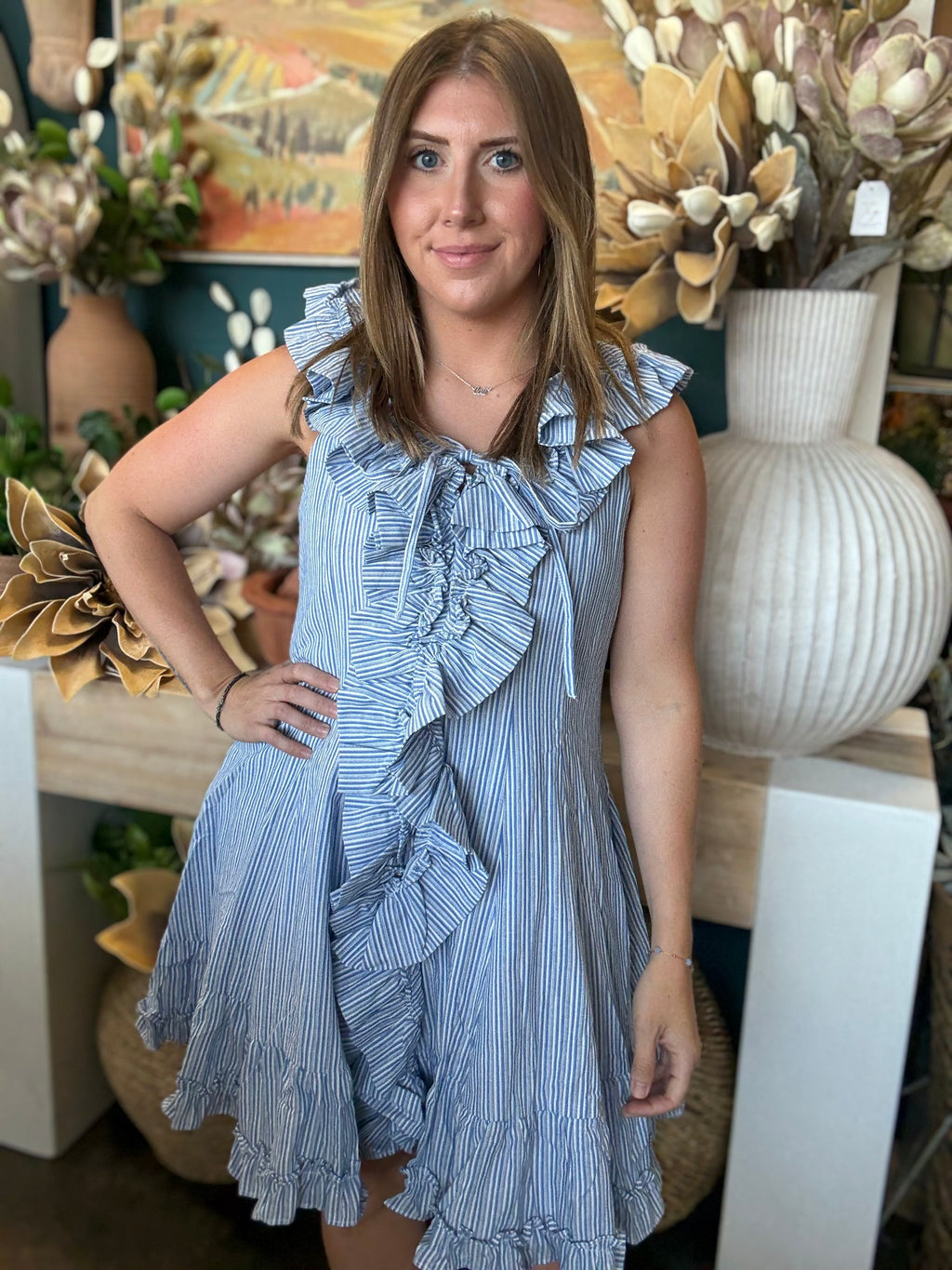 Woman wearing a blue and ivory pinstripe sleeveless mini dress with cascading front ruffles and a tie neckline