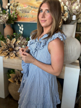 Woman wearing a blue and ivory pinstripe sleeveless mini dress with cascading front ruffles and a tie neckline