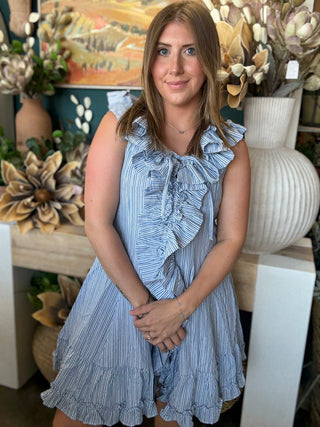 Woman wearing a blue and ivory pinstripe sleeveless mini dress with cascading front ruffles and a tie neckline