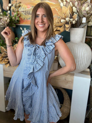 Woman wearing a blue and ivory pinstripe sleeveless mini dress with cascading front ruffles and a tie neckline