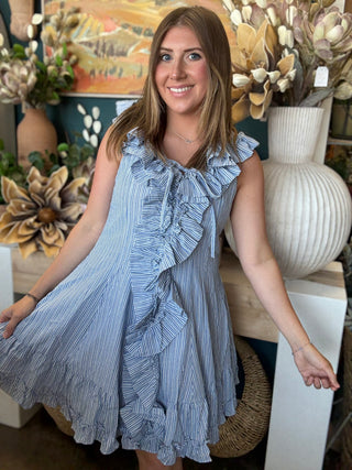 Woman wearing a blue and ivory pinstripe sleeveless mini dress with cascading front ruffles and a tie neckline