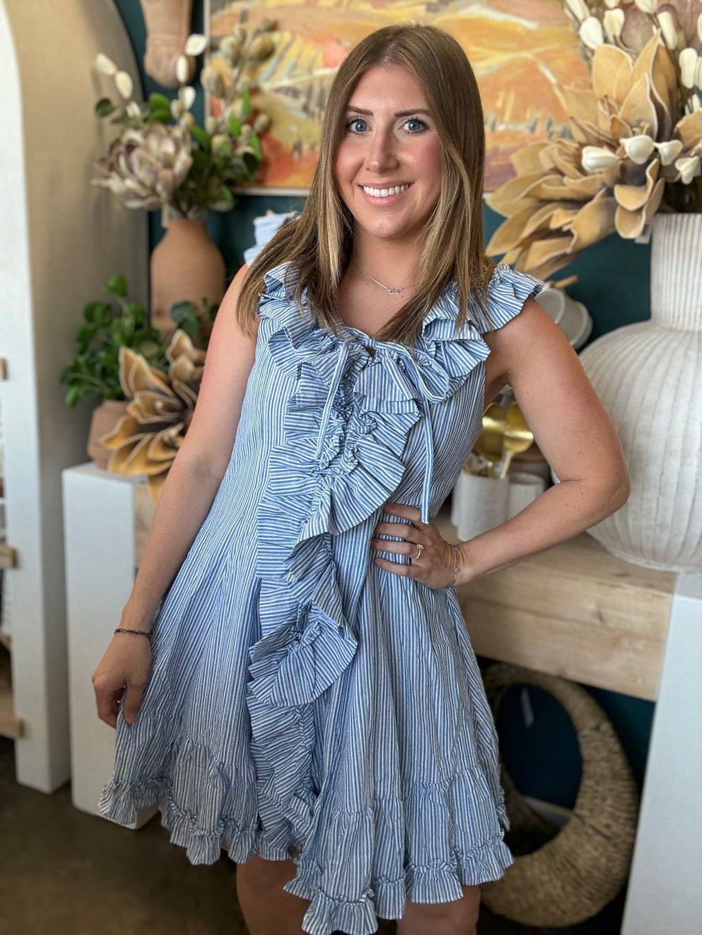 Woman wearing a blue and ivory pinstripe sleeveless mini dress with cascading front ruffles and a tie neckline