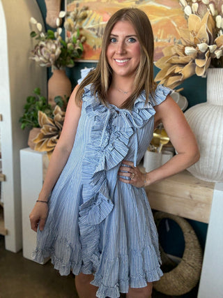 Woman wearing a blue and ivory pinstripe sleeveless mini dress with cascading front ruffles and a tie neckline
