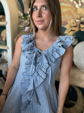 Woman wearing a blue and ivory pinstripe sleeveless mini dress with cascading front ruffles and a tie neckline