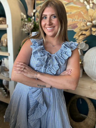 Woman wearing a blue and ivory pinstripe sleeveless mini dress with cascading front ruffles and a tie neckline