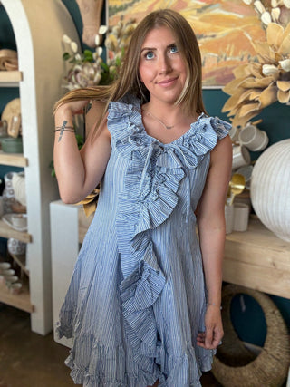 Woman wearing a blue and ivory pinstripe sleeveless mini dress with cascading front ruffles and a tie neckline
