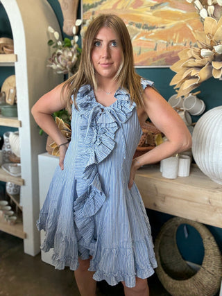 Woman wearing a blue and ivory pinstripe sleeveless mini dress with cascading front ruffles and a tie neckline