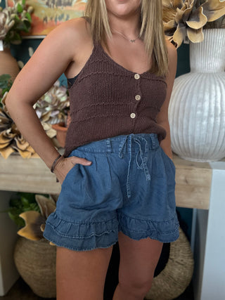 Woman wearing chambray blue ruffle hem shorts with an elastic drawstring waistband and side pockets