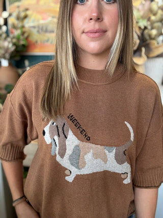 Woman wearing a camel brown knit sweater with an embroidered dog graphic and Weekend lettering