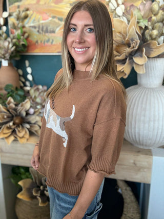 Woman wearing a camel brown knit sweater with an embroidered dog graphic and Weekend lettering