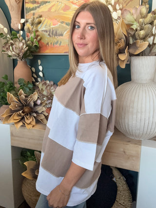 Woman wearing an oversized mocha and white color block short sleeve knit top with light wash jeans