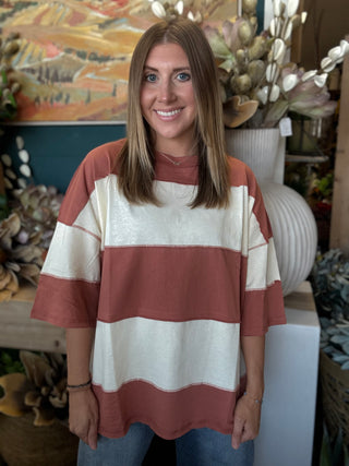 Woman wearing an oversized toasted almond and ivory color block knit top with medium wash jeans
