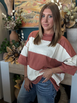 Woman wearing an oversized toasted almond and ivory color block knit top with medium wash jeans