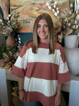 Woman wearing an oversized toasted almond and ivory color block knit top with medium wash jeans