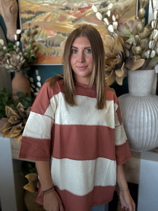 Woman wearing an oversized toasted almond and ivory color block knit top with medium wash jeans