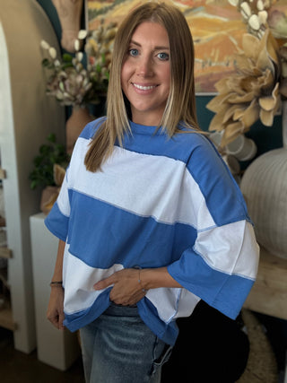 Woman wearing an oversized sky blue and white color block knit top with light wash jeans