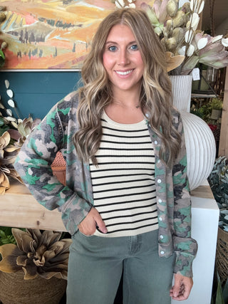 Woman wearing a lightweight faded camouflage button-front cardigan layered over a striped knit tank