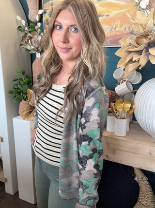 Woman wearing a lightweight faded camouflage button-front cardigan layered over a striped knit tank