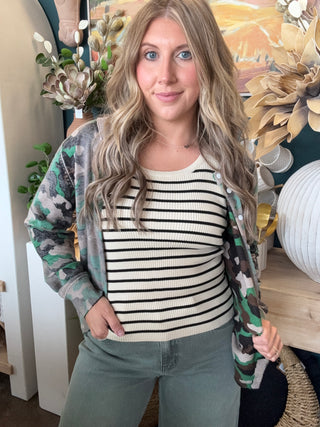 Woman wearing a lightweight faded camouflage button-front cardigan layered over a striped knit tank