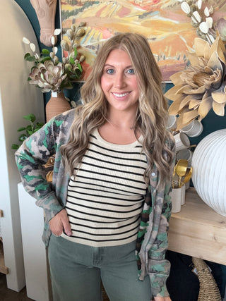 Woman wearing a lightweight faded camouflage button-front cardigan layered over a striped knit tank