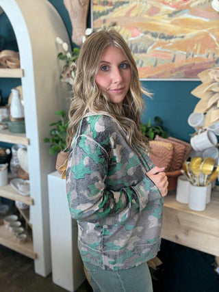 Woman wearing a lightweight faded camouflage button-front cardigan layered over a striped knit tank