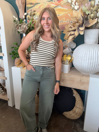Woman wearing a fitted cream and black striped sleeveless ribbed knit top with olive green pants