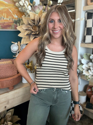 Woman wearing a fitted cream and black striped sleeveless ribbed knit top with olive green pants