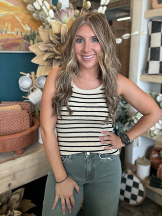 Woman wearing a fitted cream and black striped sleeveless ribbed knit top with olive green pants