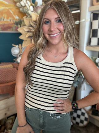 Woman wearing a fitted cream and black striped sleeveless ribbed knit top with olive green pants